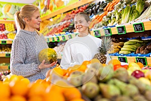 Smiling teenage girl with mother choosing fruits and vegetables in supermarket