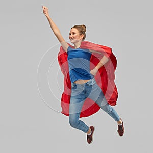 Smiling teenage girl in red superhero cape jumping