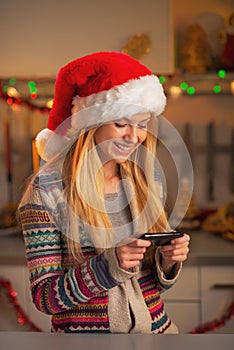 Smiling teenage girl in santa hat writing sms in kitchen