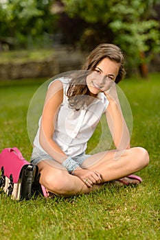 Smiling teenage girl sitting grass with satchel