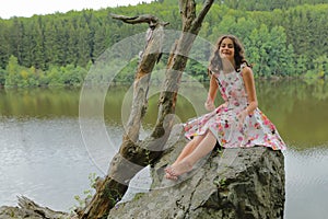 Smiling teenage girl sitting on rock above river