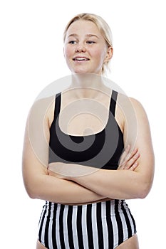 A smiling teenage girl in a sports swimsuit stands with her arms crossed over her chest. A cute blonde with freckles on her face