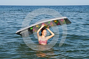 Smiling teenage girl standing in the sea and holding an inflatable mattress in her hands above her head