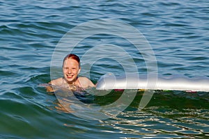 Smiling teenage girl swims with inflatable mattress in the sea