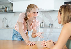 Smiling teenage girl talking friendly with woman in home kitchen