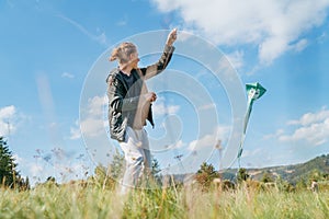 Smiling teenager boy with flying colorful kite on the high grass meadow in the mountain fields. Happy childhood moments or outdoor