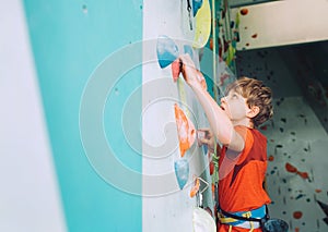 Smiling teenager boy at indoor climbing wall hall. The boy is climbing using a top rope and climbing harness. Active teenager time