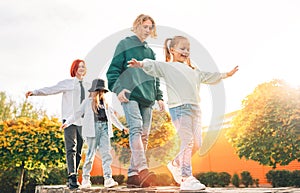 Smiling teenager boy and a laughing sisters girls kids walking in row in the autumnal sunny city park.Careless young teenhood time