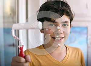 Smiling teenager boy with white paint roller and dirty face make repaint