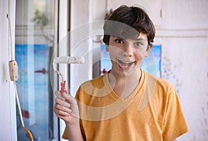 Smiling teenager boy with white paint roller and dirty face make repaint