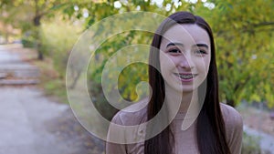 Smiling teenager girl with braces looking around and at the camera outside