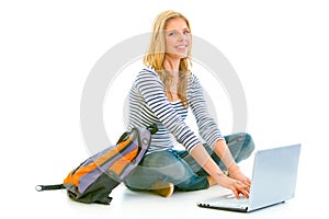 Smiling teengirl sitting on floor and using laptop