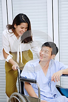 Smiling Thai woman is Caring and Take the old father sitting on wheelchair and ill health for to see a doctor at hospital.