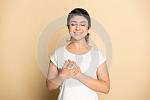 Smiling thankful Indian woman hold hands at heart