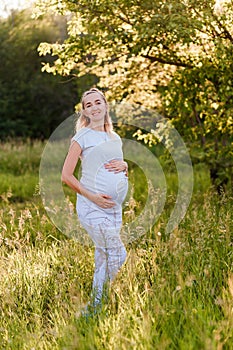 A smiling thirty-year-old pregnant woman in a gray t-shirt holds her hands on her stomach. nine months, waiting for a baby. happy