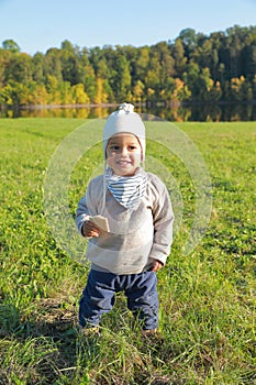 Smiling toddler boy with bread in autumn clothes on meadow