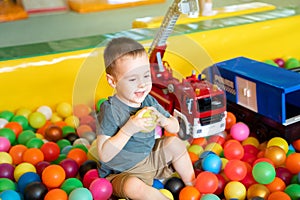 Smiling toddler boy playing with balls in children\'s playroom.