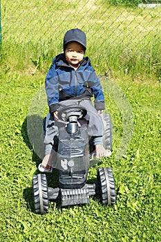 Smiling toddler boy playing on playground - riding black tractor