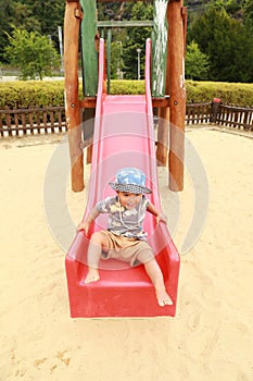 Smiling toddler boy playing on playground - sliding red slide