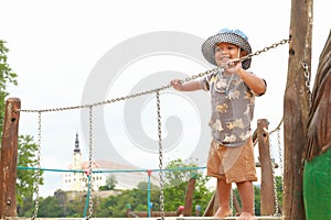 Smiling toddler boy playing on playground - standing on bridge