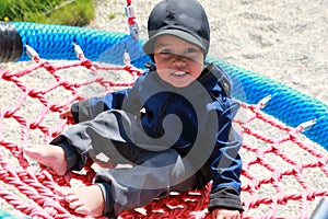 Smiling toddler boy playing on playground - swinging on net swing