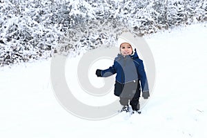 Smiling toddler boy in snow by bush