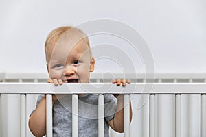 Smiling toddler standing in the bed and holds by the cot rails