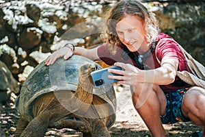 Smiling tourist boy making a selfie using cell phone with Aldabra giant tortoise endemic species - one of the largest tortoises in photo