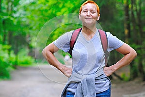 A smiling tourist girl stands on a forest path. A backpack is slung over his shoulders