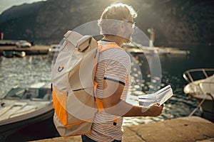Tourist mature man standing with map and backpack near the sea
