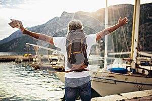 Tourist mature man standing with map and backpack near the sea