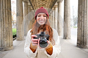 Smiling tourist photographer, takes picture during her trip, holds professional camera and makes photos