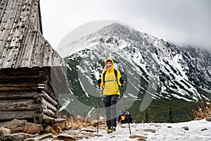 Smiling tourist woman in down jacket hiking with nordic walking poles on trail in beautiful mountains.