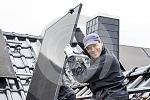 Smiling tradesman installing a solar panel on a roof of a house