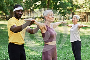 Smiling trainer assisting senior woman working out outdoors in park