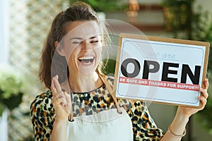 Smiling trendy business owner woman in apron showing open sign