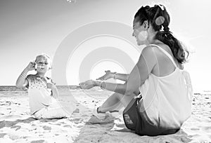 Smiling trendy mother and child on seacoast blowing bubbles