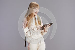 smiling trendy teenage girl in beige tracksuit using tablet PC