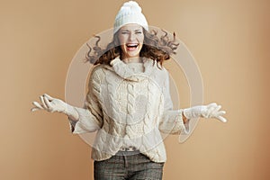 smiling trendy woman in beige sweater, mittens and hat jumping