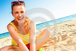 Smiling trendy woman in colorful dress sitting on beach