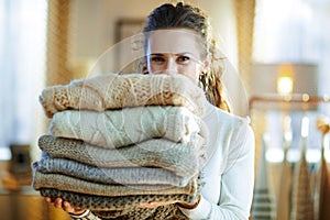 Smiling trendy woman holding pile of sweaters