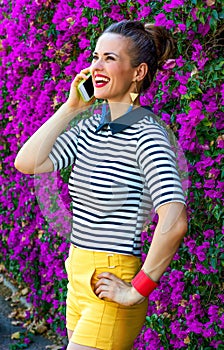 Smiling trendy woman near flowers bed speaking on cell phone