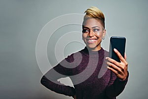 Smiling trendy young woman looking to side at copy space while holding her smart phone