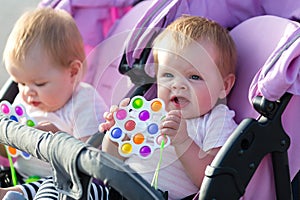 Smiling twin girls in a baby carriage with bright toys