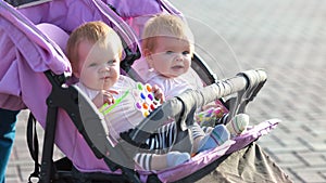 Smiling twin girls in baby carriage with bright toys