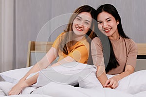 Smiling Two Asian young  lovely couple sitting on white bed and happy.  Funny women after wake up together on cozy. Concept In