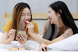 Smiling Two Asian young  women lovely couple repose on white bed and happy Feed apples. Funny women together on cozy. Concept In