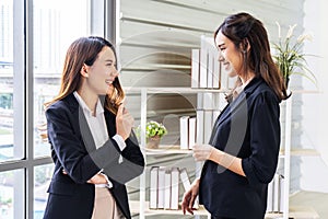 Smiling two business woman talking with partner while standing in modern office interior, team of professional employees