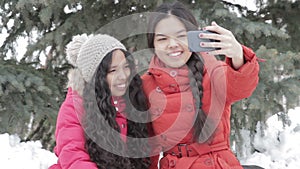 Smiling two girl taking a selfie with smartphone outdoors in warm clothes