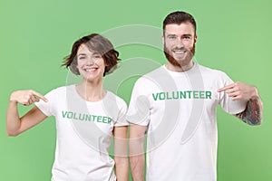 Smiling two young friends couple in white volunteer t-shirt isolated on pastel green background. Voluntary free work